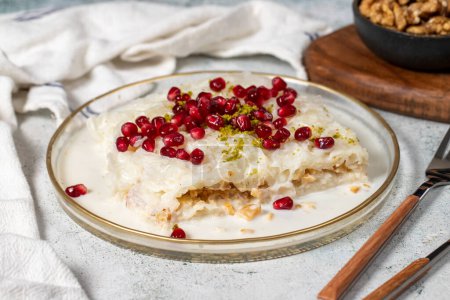 Dessert Gullac. Dessert du Ramadan. Gullac garni de grenade et pistache en plaque de verre sur fond gris. Alimentation symbolique.