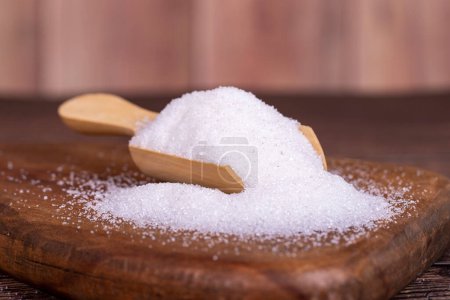 Foto de Azúcar blanco refinado sobre fondo de madera. Primer plano del azúcar granulado en cuchara de madera - Imagen libre de derechos
