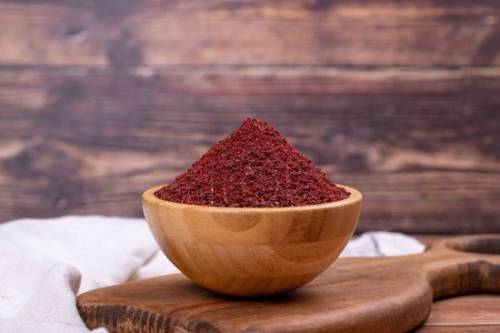 Sumac on wooden background. Dried ground red Sumac powder spices in wooden bowl