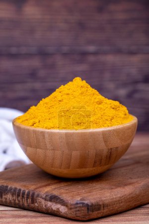 Photo for Powdered turmeric on wooden background. Dried ground turmeric powder spices in wooden bowl. Close up - Royalty Free Image