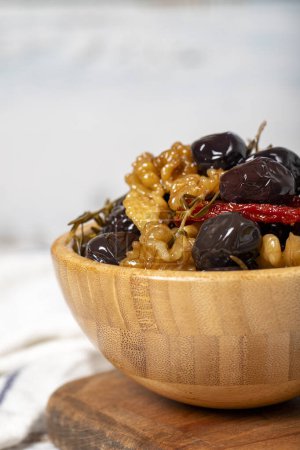 Téléchargez les photos : Mélanger les olives avec les olives noires, les noix, les tomates séchées et le thym dans un bol en bois. Oliviers sur fond de bois blanc. Nourriture méditerranéenne. nourriture végétalienne. Gros plan - en image libre de droit