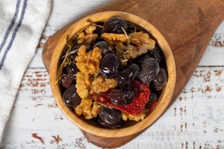 Téléchargez les photos : Mélanger les olives avec les olives noires, les noix, les tomates séchées et le thym dans un bol en bois. Oliviers sur fond de bois blanc. Nourriture méditerranéenne. nourriture végétalienne. Vue du dessus - en image libre de droit