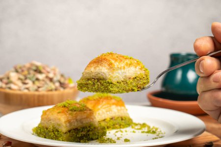 Foto de Baklava con pistachos sobre un fondo de madera. Delicias de cocina turca. Postre del Ramadán. Está sosteniendo una rebanada de baklava en el tenedor. nombre local kuru baklava - Imagen libre de derechos