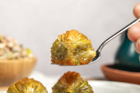 Muschelbaklava mit Pistazien auf einem hölzernen Hintergrund. Türkische Spezialitäten. Ramadan-Dessert. Er hält eine Scheibe Baklava auf der Gabel