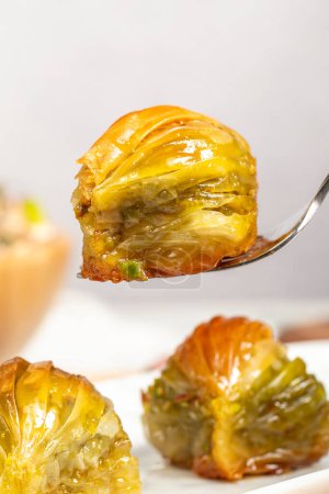 Mussel baklava with pistachios on a wooden background. Turkish cuisine delicacies. Ramadan Dessert. He is holding a slice of baklava on the fork
