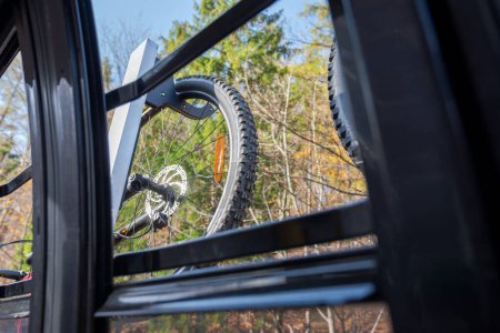 Das Rad eines Mountainbikes hängt außerhalb des Wagens einer Bergbahn, gesehen durch das geöffnete Fenster der Gondel. Schöner Herbst, sonniger Tag. Abenteuerzeit. 