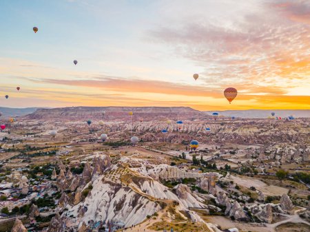 Téléchargez les photos : Aventureux vacances d'été occasion pour les touristes. Lever de soleil chaud et coloré illuminant le ciel avec des montgolfières survolant la Cappadoce, Turquie. Photo de haute qualité - en image libre de droit
