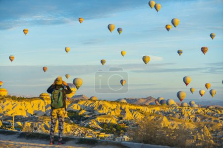 Téléchargez les photos : 10.11.2022 Cappadoce, Turquie. Destinations touristiques en Asie de l'Ouest. Touriste aléatoire méconnaissable debout à l'arrière de l'appareil photo et de prendre des photos d'une vue imprenable et inhabituelle des dizaines d'air chaud - en image libre de droit