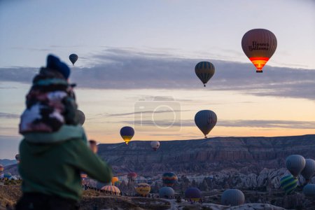Téléchargez les photos : 10.11.2022 Cappadoce, Turquie. Un parent flou tenant son enfant cochon au premier plan, regardant de superbes ballons colorés au-dessus de la ville turque de Cappadoce. Photo de haute qualité - en image libre de droit