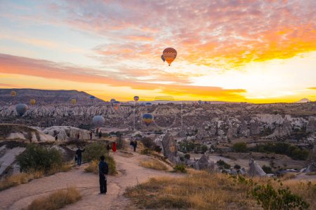 Téléchargez les photos : 10.11.2022 Cappadoce, Turquie. Lever de soleil coloré avec une belle formation de nuages en Cappadoce. Touristes méconnaissables debout sur la colline, admirant une belle vue et des montgolfières volant à travers - en image libre de droit