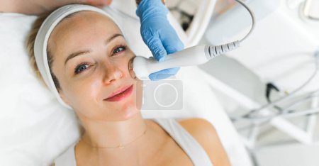 SPA treatment day. Closeup indoor portrait of lying attractive caucasian woman during microdermabrasion procedure performed by professional unrecognizable cosmetician. High quality photo