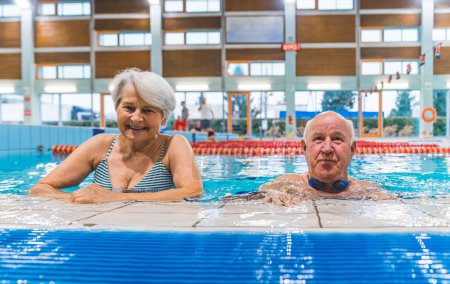 Foto de Mayores en una piscina. Retrato de dos pensionistas caucásicos - una mujer y un hombre - mirando a la cámara mientras están de pie cerca del borde de una piscina. Foto de alta calidad - Imagen libre de derechos