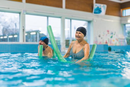 Photo for Variety of swimming equipment. Green foam noodles used by active happy caucasian senior couple. Swimming pool interior. High quality photo - Royalty Free Image