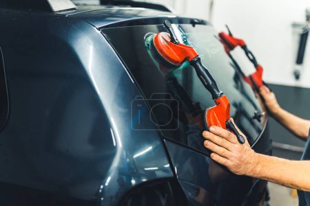 Photo for Indoor closeup shot of unrecognizable caucasian mechanic using suction cups for car windows to remove rear window from black car. High quality photo - Royalty Free Image
