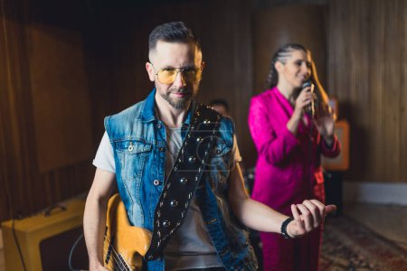 Photo for Medium shot of a young guitarist man with yellow sunglasses, a young woman in a pink suit singing in the background. High quality photo - Royalty Free Image