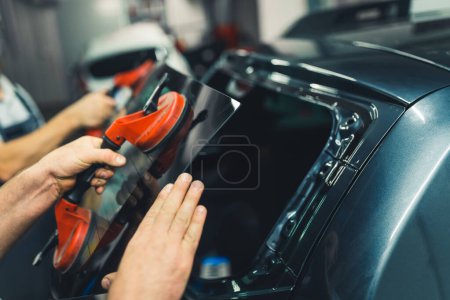 Photo for Windshield or rear window removal with the use of suction cups. Indoor closeup portrait. Two caucasian unrecognizable mechanics repairing a vehicle. High quality photo - Royalty Free Image
