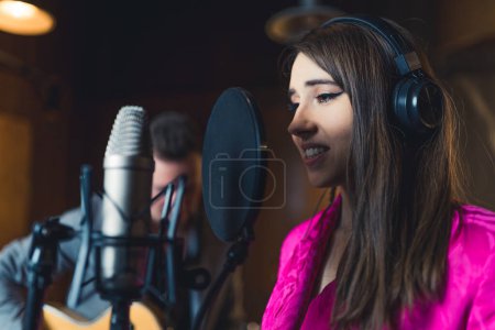 Sänger nimmt neuen Song auf. Innenporträt einer braunhaarigen kaukasischen Sängerin, die zum Mikrofon singt. Band-Konzept. Hochwertiges Foto