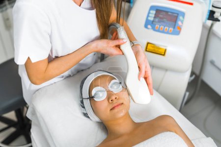 Foto de High-angle shot of a woman lating down and receiving an Erbium-yag fractional laser face treatment being done by a beautician. Beauty concept. High quality photo - Imagen libre de derechos