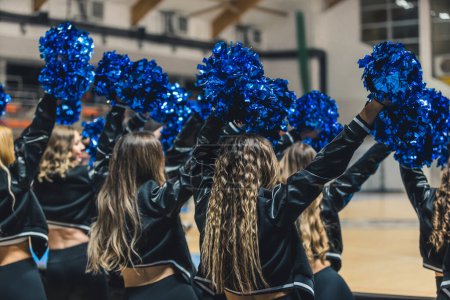 Téléchargez les photos : A group of cheerleaders are captured in mid-performance, their blue pom-poms waving in the air as they cheer on their team during a match. The young women are full of energy and excitement. - en image libre de droit