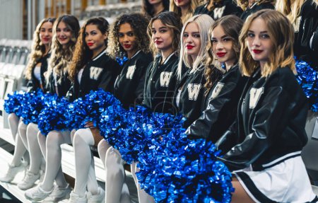 Téléchargez les photos : Cheerleaders sitting on chairs in a row dressed in mini-skirts holding pom-poms. - en image libre de droit