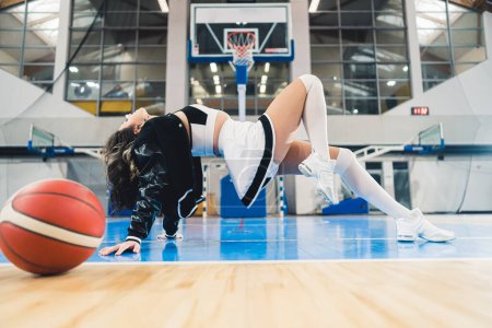 Foto de Cheerleader displays felxibility in athletic pose a basketball is placed nearby. High quality photo - Imagen libre de derechos