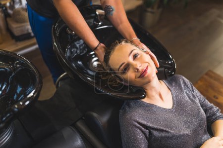 Photo for Hairdresser washing clients hair and client smiling at the camera, medium shot beauty salon. High quality photo - Royalty Free Image