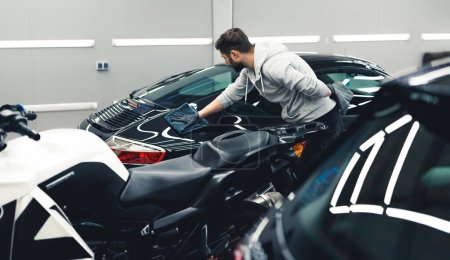 Foto de Process of car detailing - applying ceramic coating - done by male professional. Black sports car car detailing. . High quality photo - Imagen libre de derechos