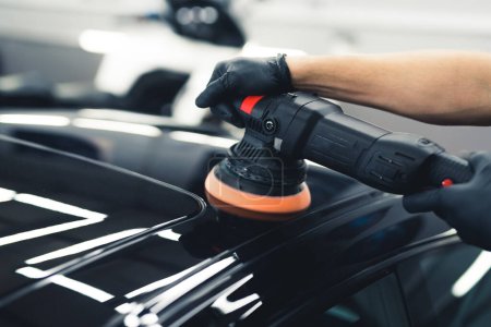 Hands of a man with orbital polisher in repair shop polishing black sports car. Closeup shot. Car detailing concept. High quality photo