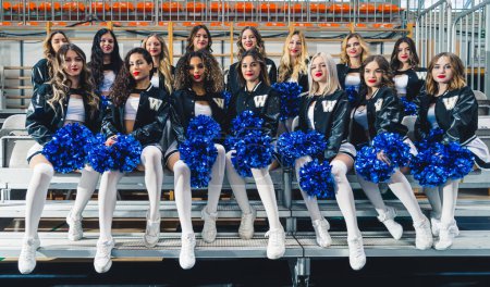 Téléchargez les photos : Female cheerleaders sitting in two rows. They are wearing black baseball hoodies. High quality photo - en image libre de droit