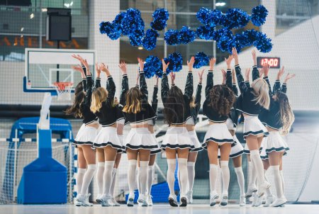 Téléchargez les photos : Dynamic photo of female cheerleader. Tossing blue pompoms above the head. They are all dressed alike. High quality photo - en image libre de droit