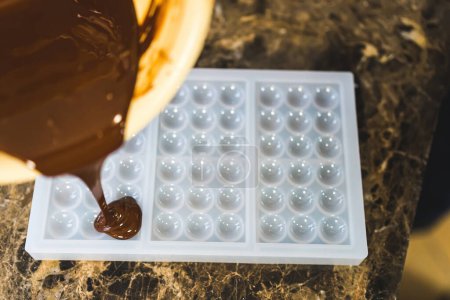 Photo for Semi-transparent mould being filled with dark milk chocolate. Process of creating home-made chocolate bars. High quality photo - Royalty Free Image