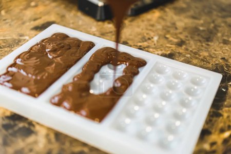 Téléchargez les photos : Chef prépare du chocolat trempé dans un moule à barres - Callets de chocolat sur le comptoir. Photo de haute qualité - en image libre de droit