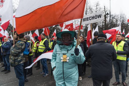 Photo for 06.03.2024. Warsaw, Poland. a beekeeper woman with uniform holding a big polish flag at the rally. High quality photo - Royalty Free Image