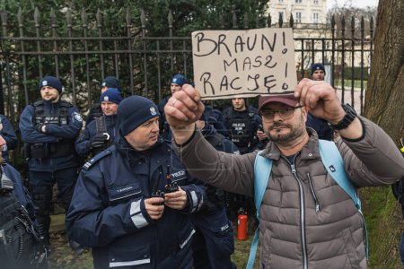 Photo for 06.03.2024. Warsaw, Poland. man from the protest showing a placard at the camera and police officers standing in the background. High quality photo - Royalty Free Image