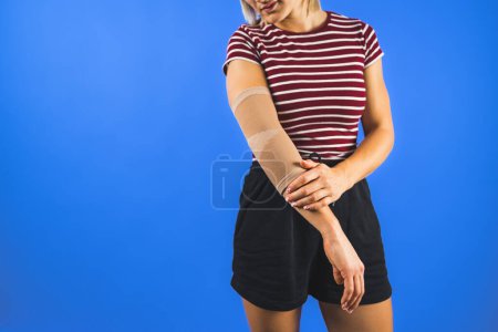 woman wearing an elbow support brace on a blue background, copy space trauma and healing concepts. High quality photo