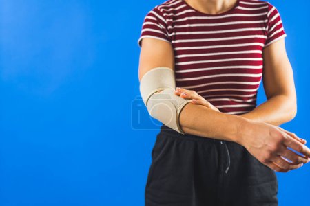cropped woman wearing elastic support elbow brace for reduce pain, blue background, copy space. High quality photo