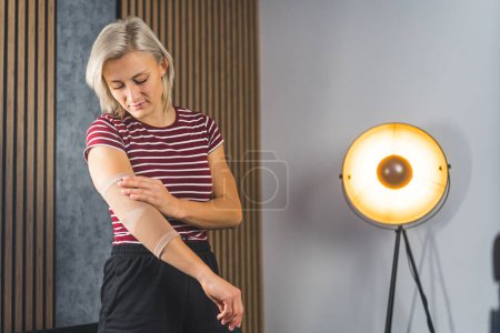 Woman with injured elbow using an elastic support, living room treatment concept. High quality photo