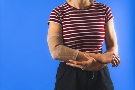 Photo for Woman wearing a bandage on her elbow, studio shot blue background. High quality photo - Royalty Free Image