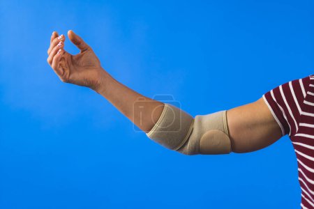 Photo for Closeup shot of a woman with brace on an injured hand over a blue background, treatment concept. High quality photo - Royalty Free Image