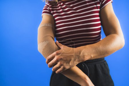 woman showing a bandage on her elbow over a blue background. High quality photo
