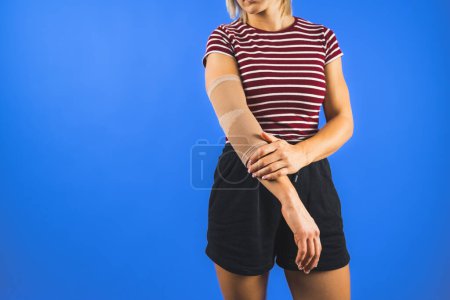 Photo for A young woman wearing an elbow support brace over a blue background, trauma concept. High quality photo - Royalty Free Image