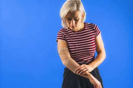 Photo for Woman wearing an elbow support brace on a blue background, copy space trauma and healing concept. High quality photo - Royalty Free Image