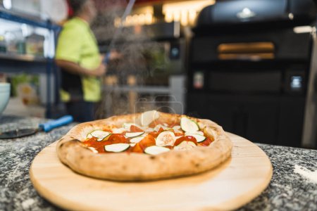 Téléchargez les photos : Pizza avec tomates et concombres sur une planche en bois, homme cuisinier en arrière-plan. Photo de haute qualité - en image libre de droit