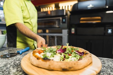 Téléchargez les photos : Chef professionnel tenant pizza avec assaisonnements, cuisine, boulangerie, technique alimentaire en arrière-plan. Photo de haute qualité - en image libre de droit