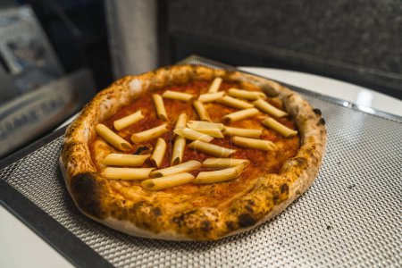Humoristisches italienisches Essenskonzept - zubereitete Pizza mit Penne Makkaroni, die traditionelle italienische Gerichte vermischt. Hochwertiges Foto