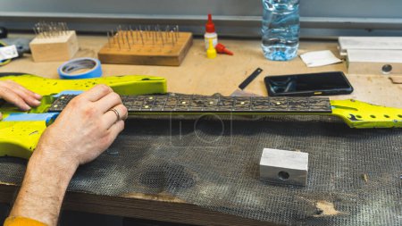 worker making the sharp fret ends smoother on the guitar, guitar manufacture. High quality photo