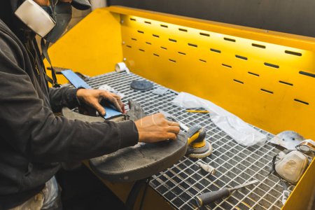 Techniker mit Maske poliert die moderne Kohlefaser-E-Gitarre in der Werkstatt. Hochwertiges Foto