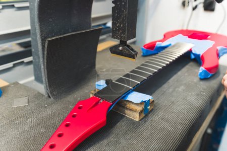 Guitarra eléctrica recién creada en la máquina, trastes de guitarra agregando máquina, taller. Foto de alta calidad
