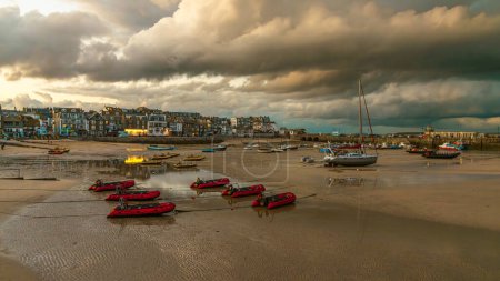 Téléchargez les photos : St Ives, Cornouailles, Angleterre, Royaume-Uni - 30 mai 2022 : Nuage sombre en soirée et bateaux dans le port à marée basse - en image libre de droit