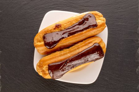 Photo for Two sweet eclairs with white plate on slate stone, macro, top view. - Royalty Free Image
